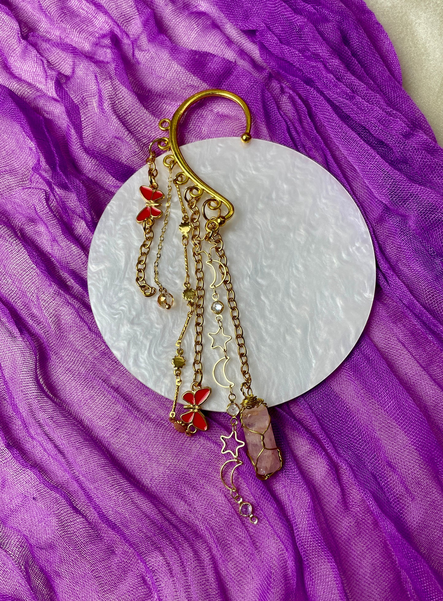 Gold ear cuff adorned with textured cactus charms, sun and moon chain, red evil eye butterfly charms, iridescent glass beads, and hand-wrapped iron-stained quartz piece, inspired by desert landscapes and celestial beauty.