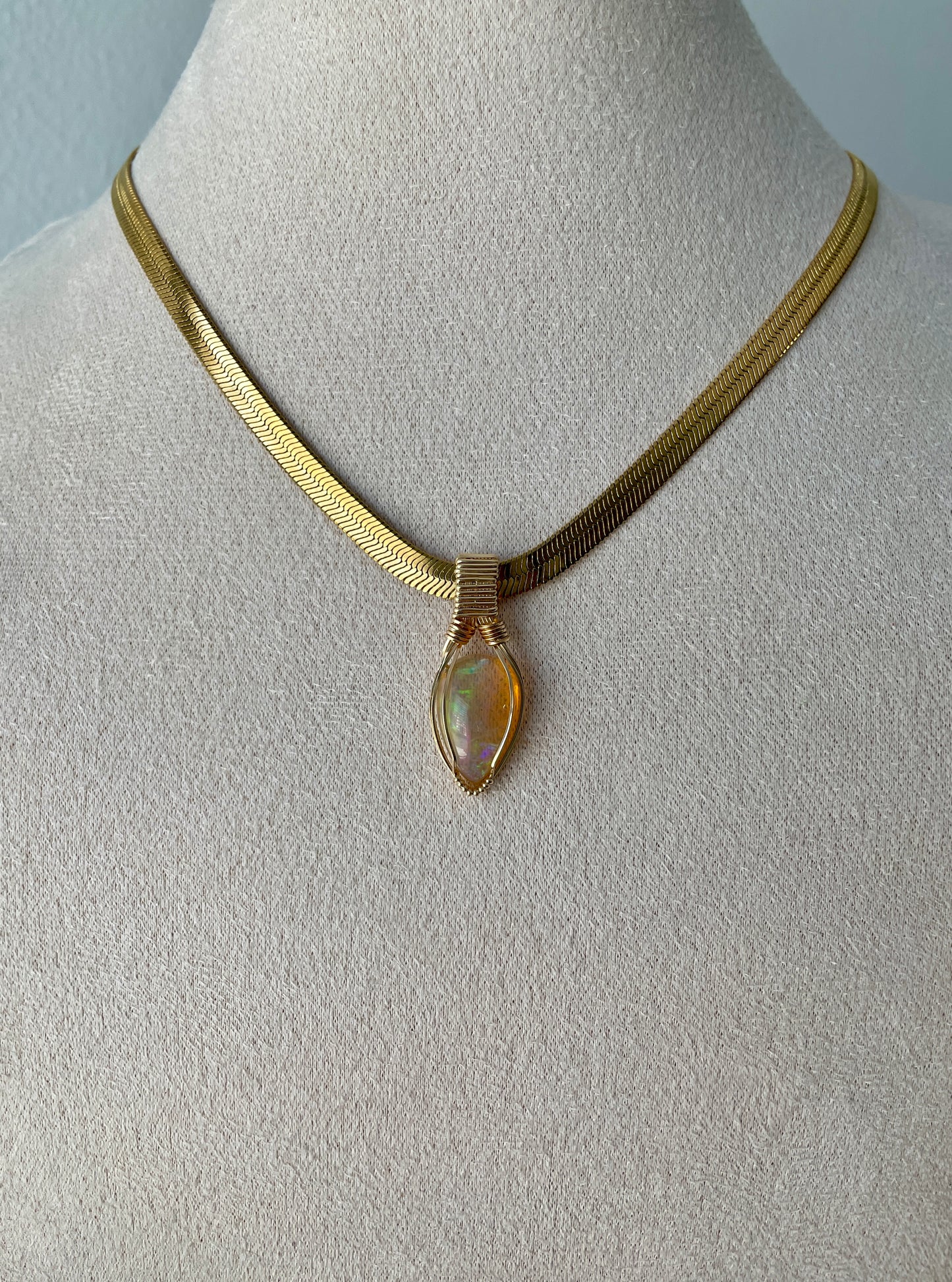 Glowing teardrop-shaped Ethiopian opal with gold wire wrapping and radiant flash, displayed on a gold vermeil flat chain.