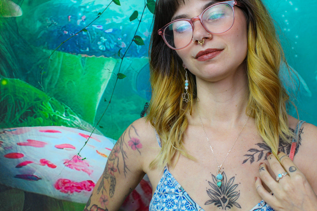 A model wearing a larimar spring ring, larimar and turquoise sterling silver pendant, and larimar lotus earrings with a magical mushroom forest backdrop.