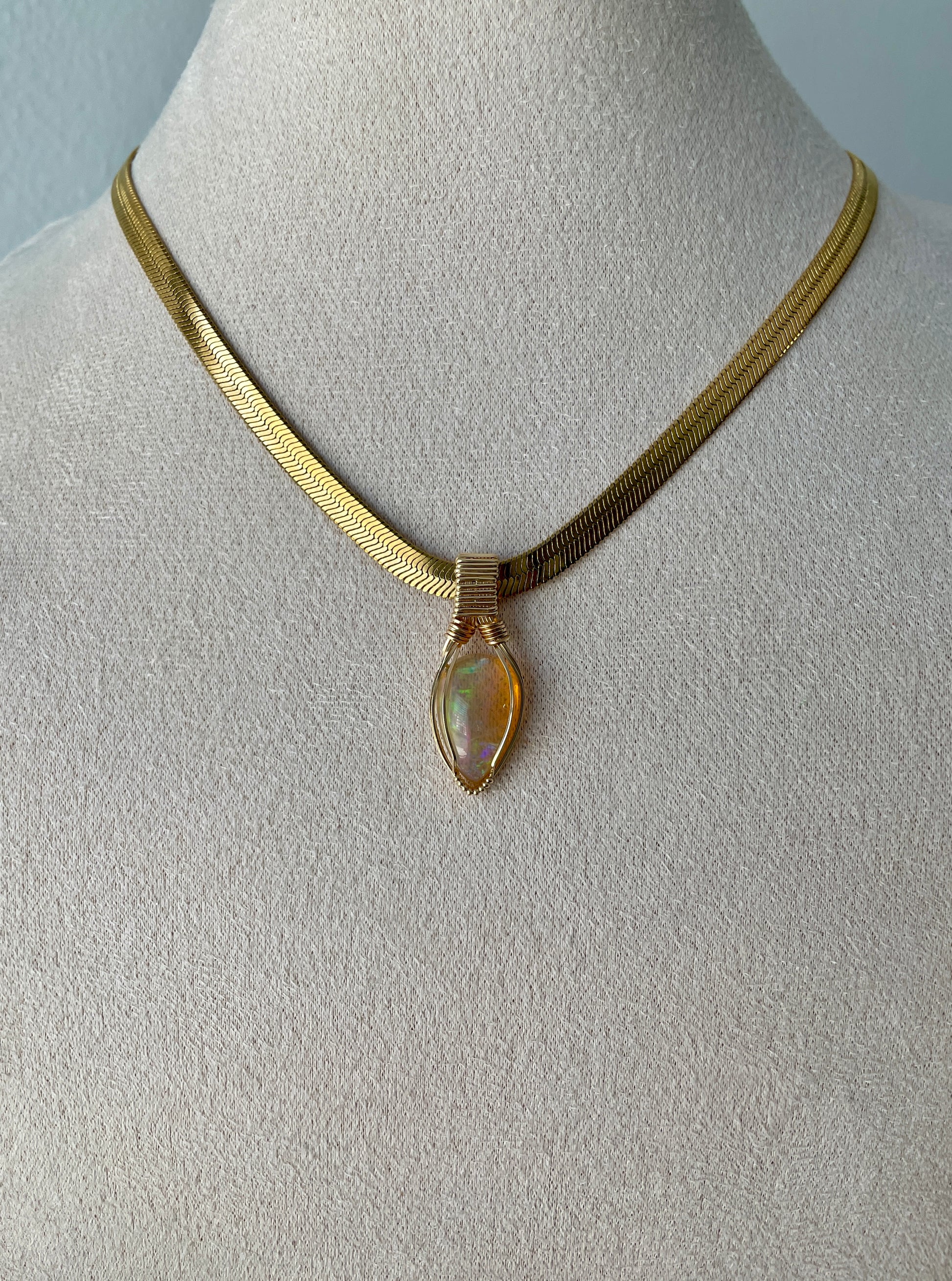 Glowing teardrop-shaped Ethiopian opal with gold wire wrapping and radiant flash, displayed on a gold vermeil flat chain.